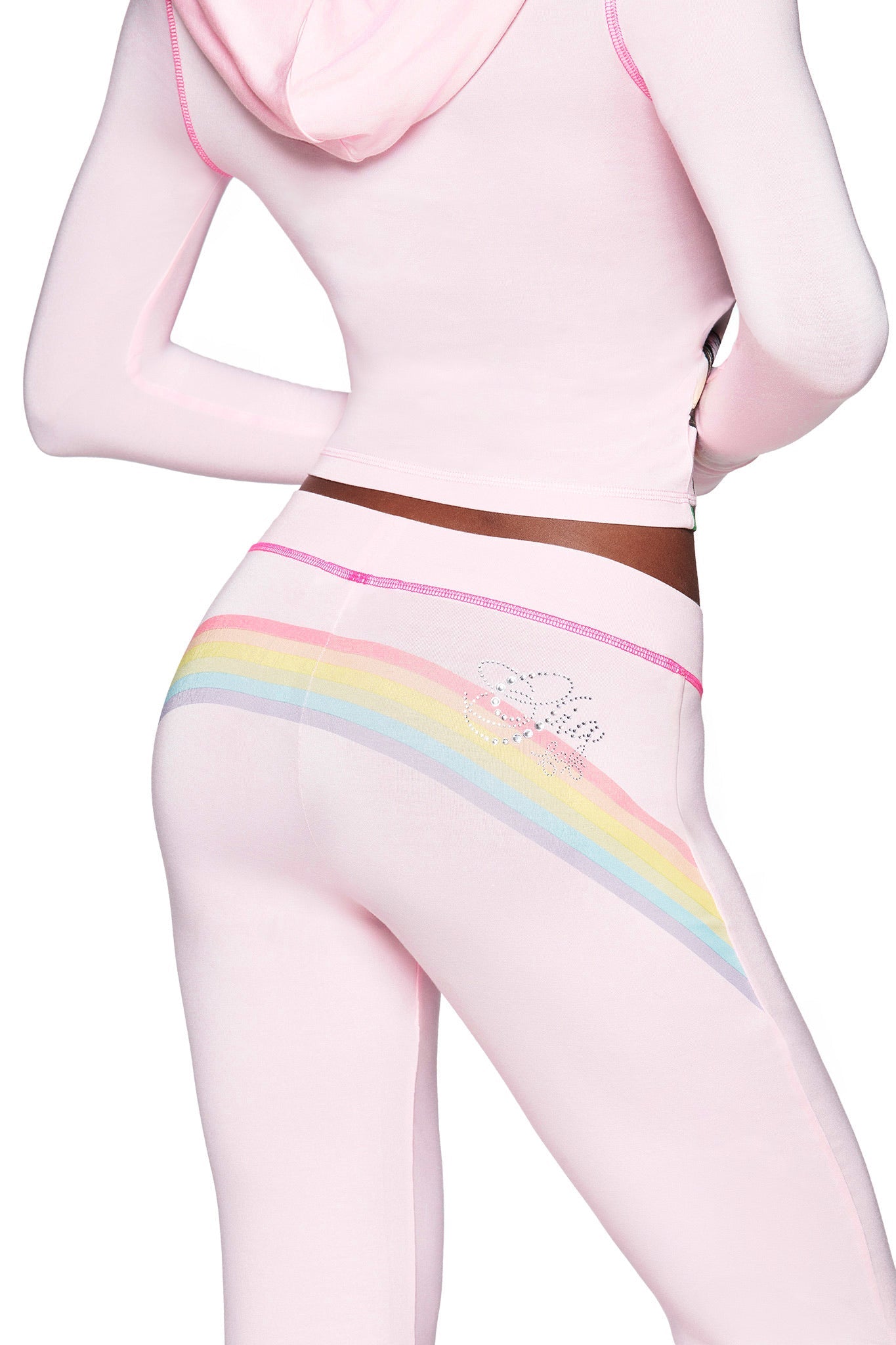 Someone wears the I.AM.GIA FAFI BLARE PANT in baby pink velour with pastel rainbow accents and rhinestones, paired with a matching cropped hoodie featuring a hood and long sleeves.