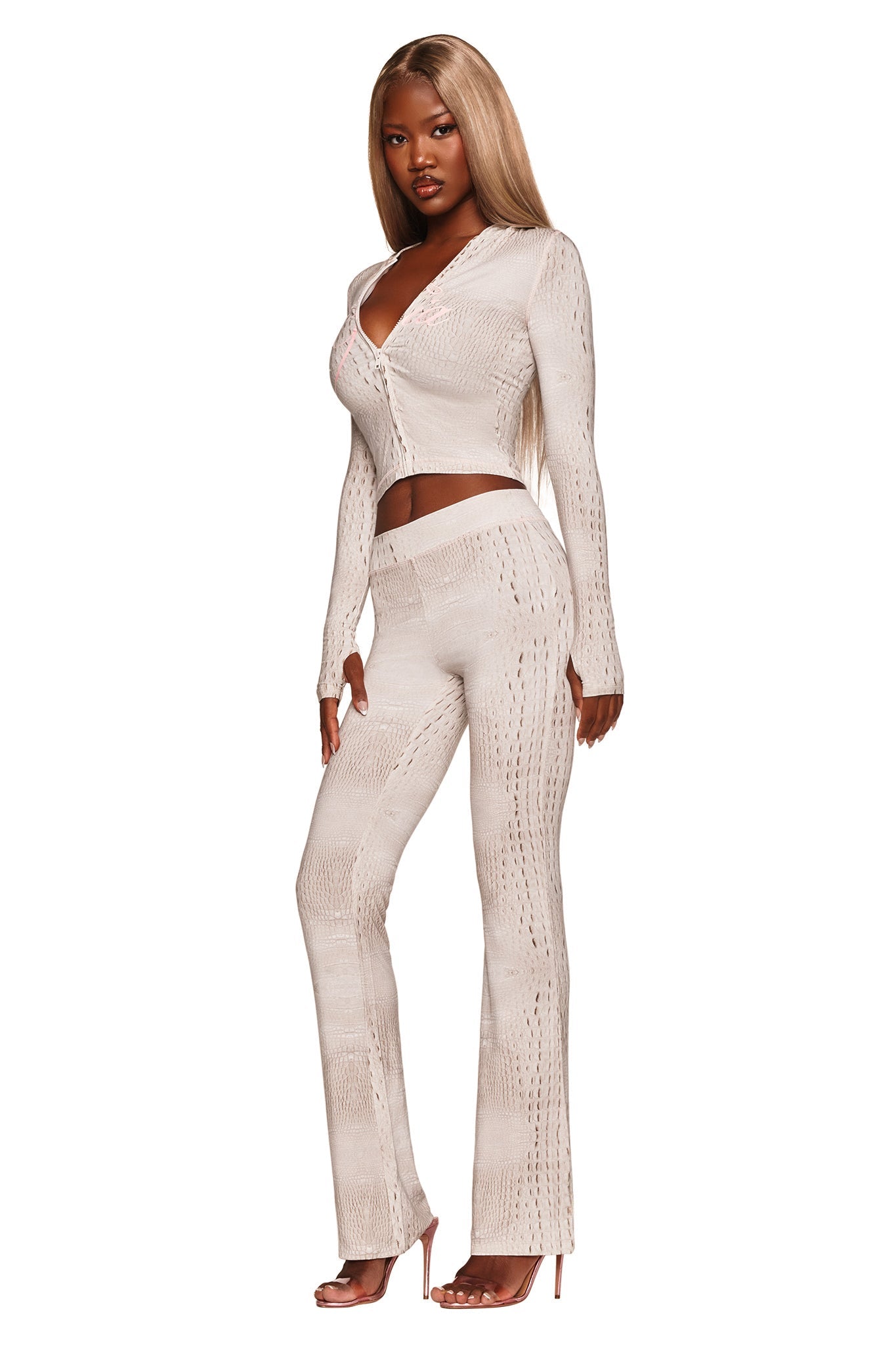 A woman with long, straight blonde hair models the I.AM.GIA BLARE TRACKPANT – HOT CROC. She wears the fitted, light beige trackpants featuring a soft bamboo fabrication and flared silhouette, paired with a matching button-up top. Standing in heels with one hand at her side and facing forward, she is set against a white background.