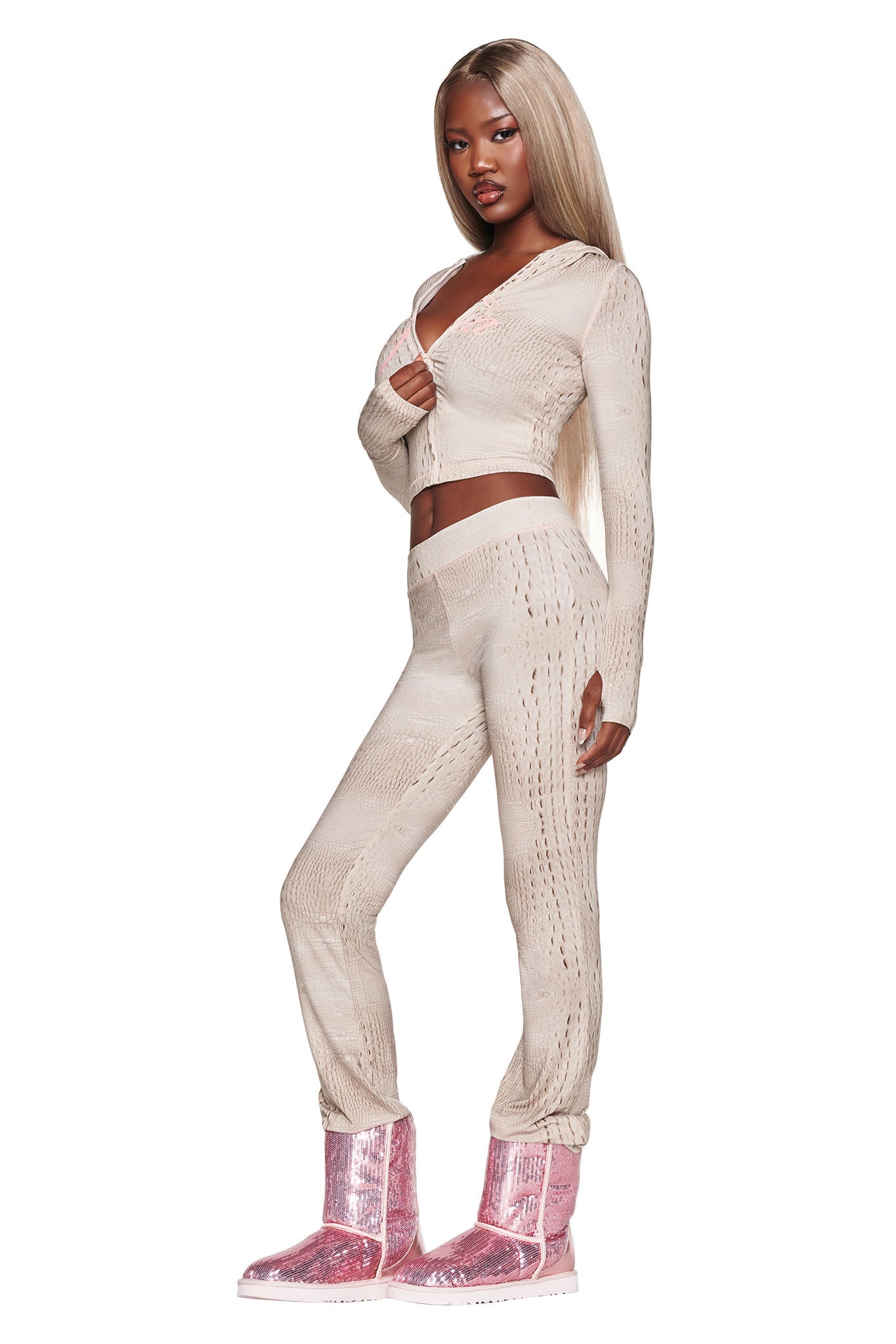 A woman with long blonde hair poses in a beige knit crop top and the BLARE TRACKPANT - HOT CROC by I.AM.GIA, crafted from soft bamboo fabrication, paired with shiny pink boots. She stands against a white background, looking confidently at the camera.