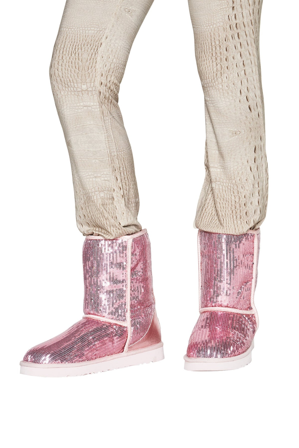 A person is wearing light textured pants paired with the I.AM.GIA ELVIRA SEQUIN BOOT in pink, featuring shiny sequins and a cozy faux fur lining.