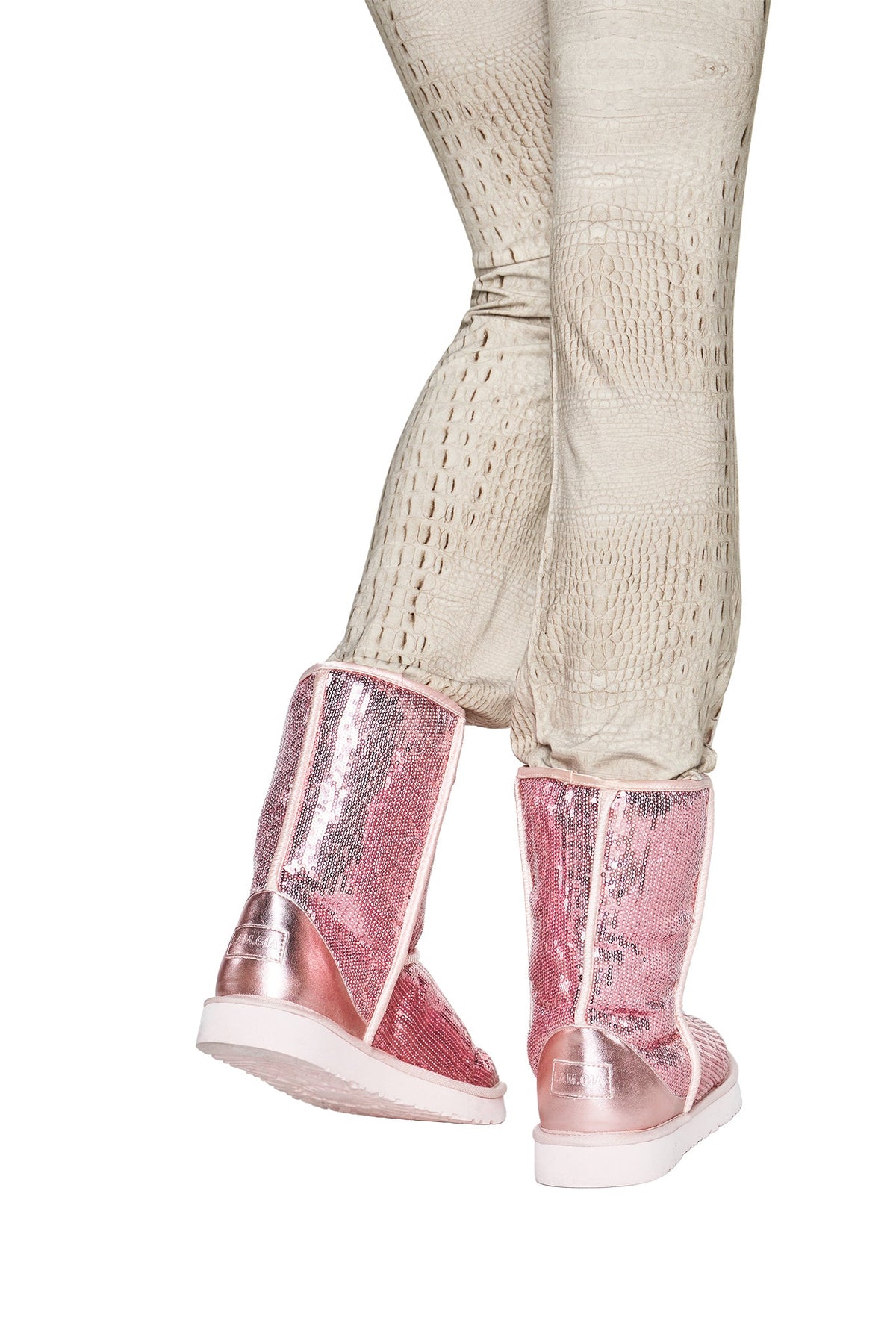 A person wearing cream textured pants and the I.AM.GIA ELVIRA SEQUIN BOOT in pink, photographed from the back against a white background.