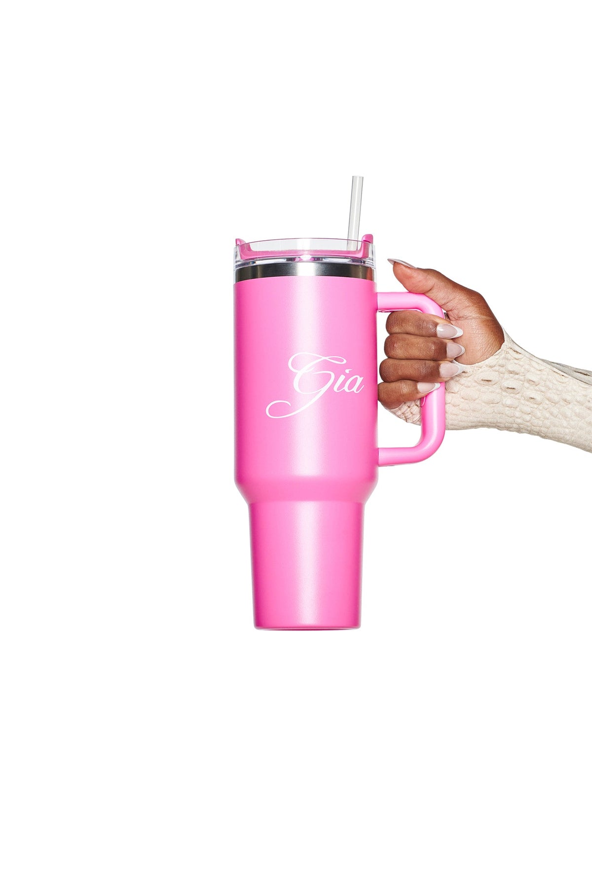 A hand holds a large hot pink BLARE CUP - PINK by I.AM.GIA, an insulated stainless steel tumbler with a straw. The name “Gia” appears in white script on the 40oz reusable cup. The person is wearing a cream-colored textured sleeve.