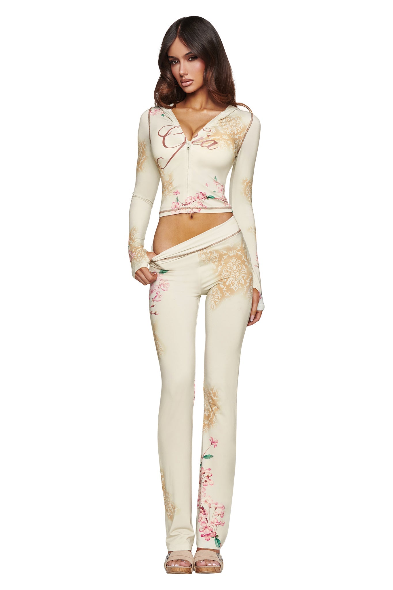 A woman poses in the BLARE HOODIE - BLOSSOM by I.AM.GIA, a cream-colored hoodie adorned with a floral print, standing against a white background and effortlessly channeling fresh elegance.