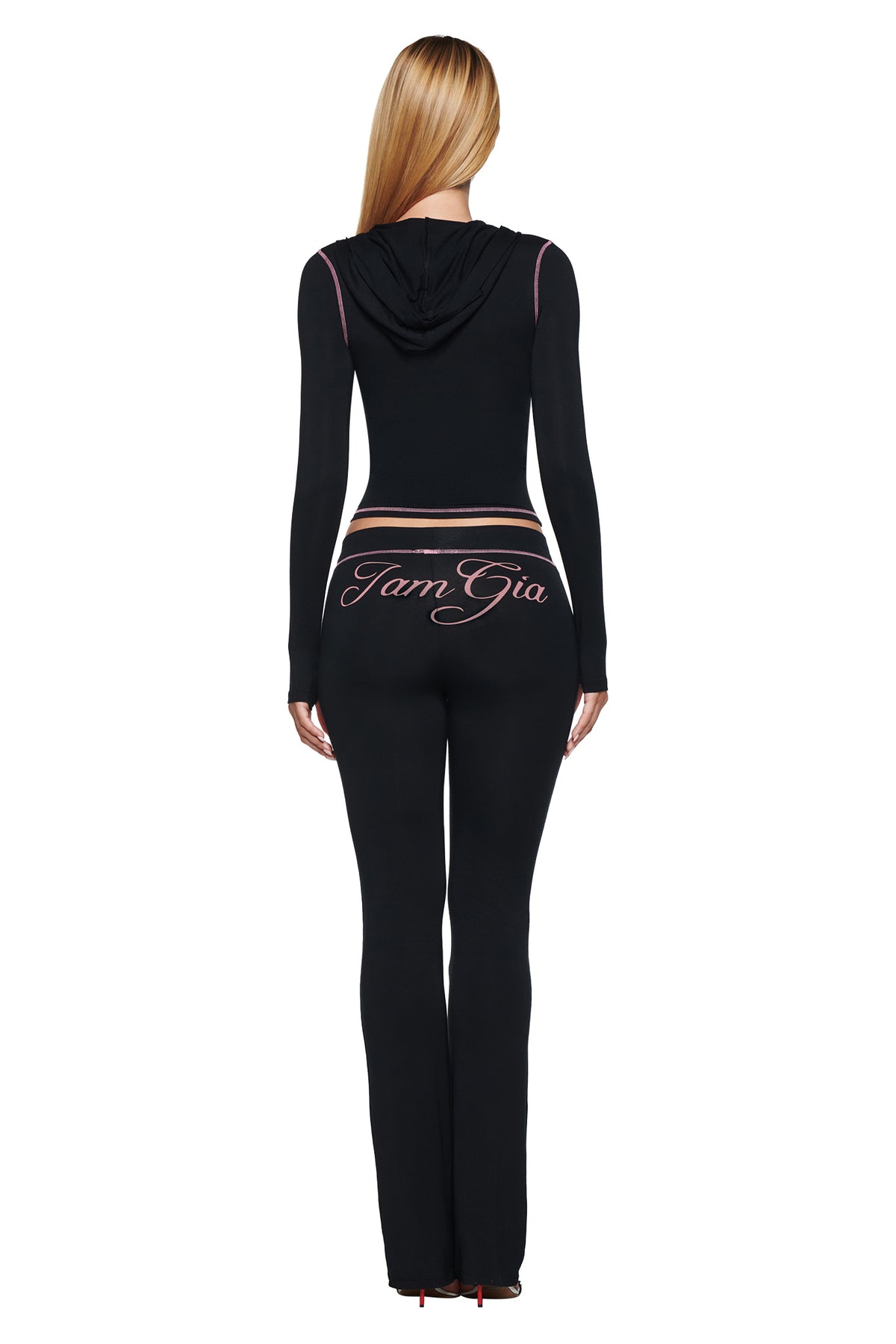 Back view of a person wearing a matching hooded top and BLARE TRACKPANT - BLACK in black, featuring pink contrast stitching and pink cursive lettering across the lower back.