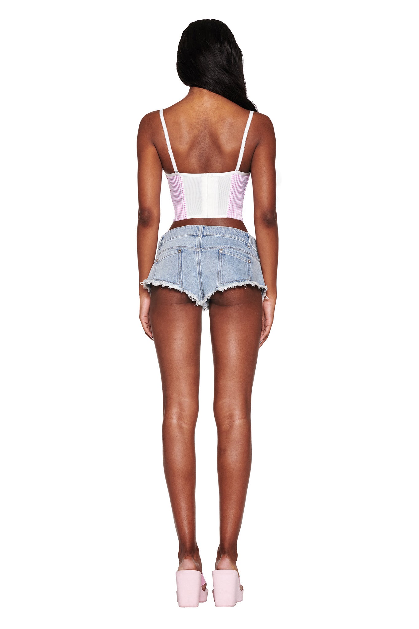 Rear view of a person with long hair wearing a pink corset top, I.AM.GIA's AURA DENIM SHORT - BLUE: LIGHT BLUE WASH, and pink platform shoes against a white background.