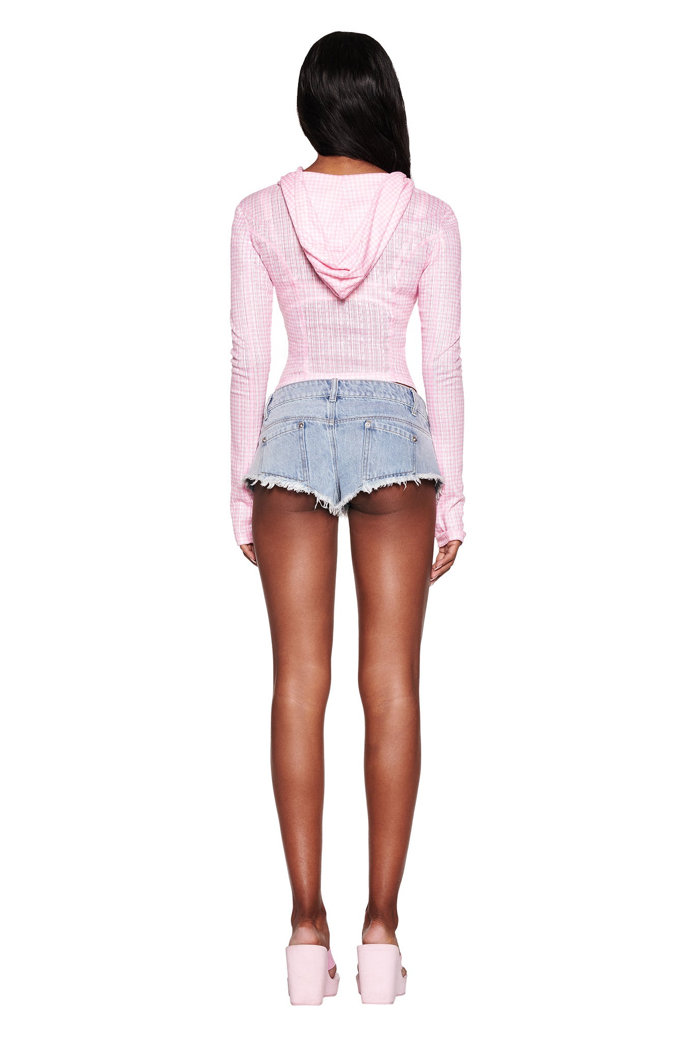 A person is seen from the rear wearing an I.AM.GIA MIA HOODIE - PINK : PINK GINGHAM with long sleeves and high-waisted frayed denim shorts, paired with pink platform shoes for a cohesive baby pink gingham look against a white backdrop.