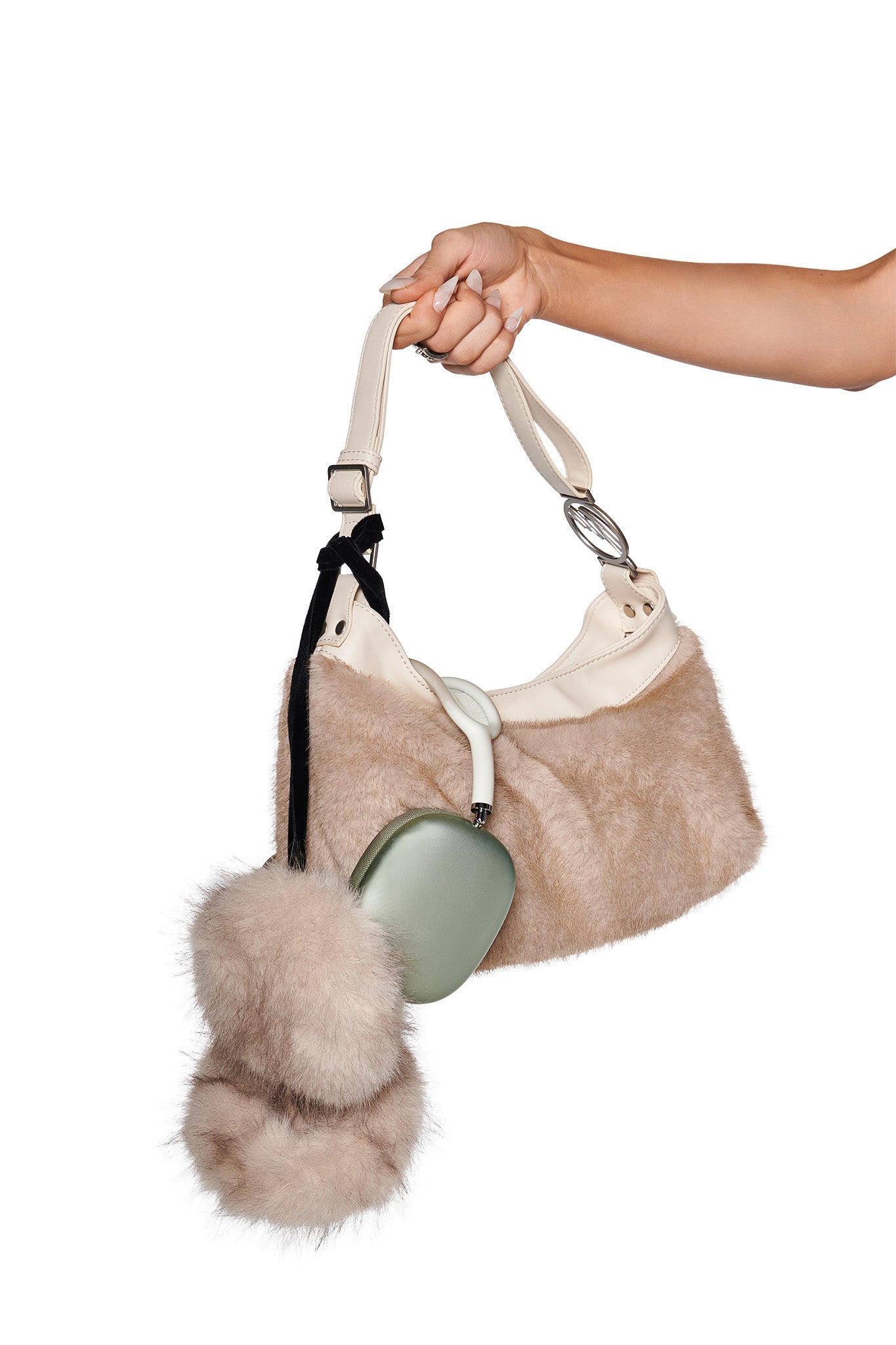 A hand holds an I.AM.GIA FAWN HEADPHONE COVERS - NEUTRAL: TAUPE, featuring soft faux fur with a large fluffy pom-pom and a green wireless earbud case attached by a black strap, set against a white background.