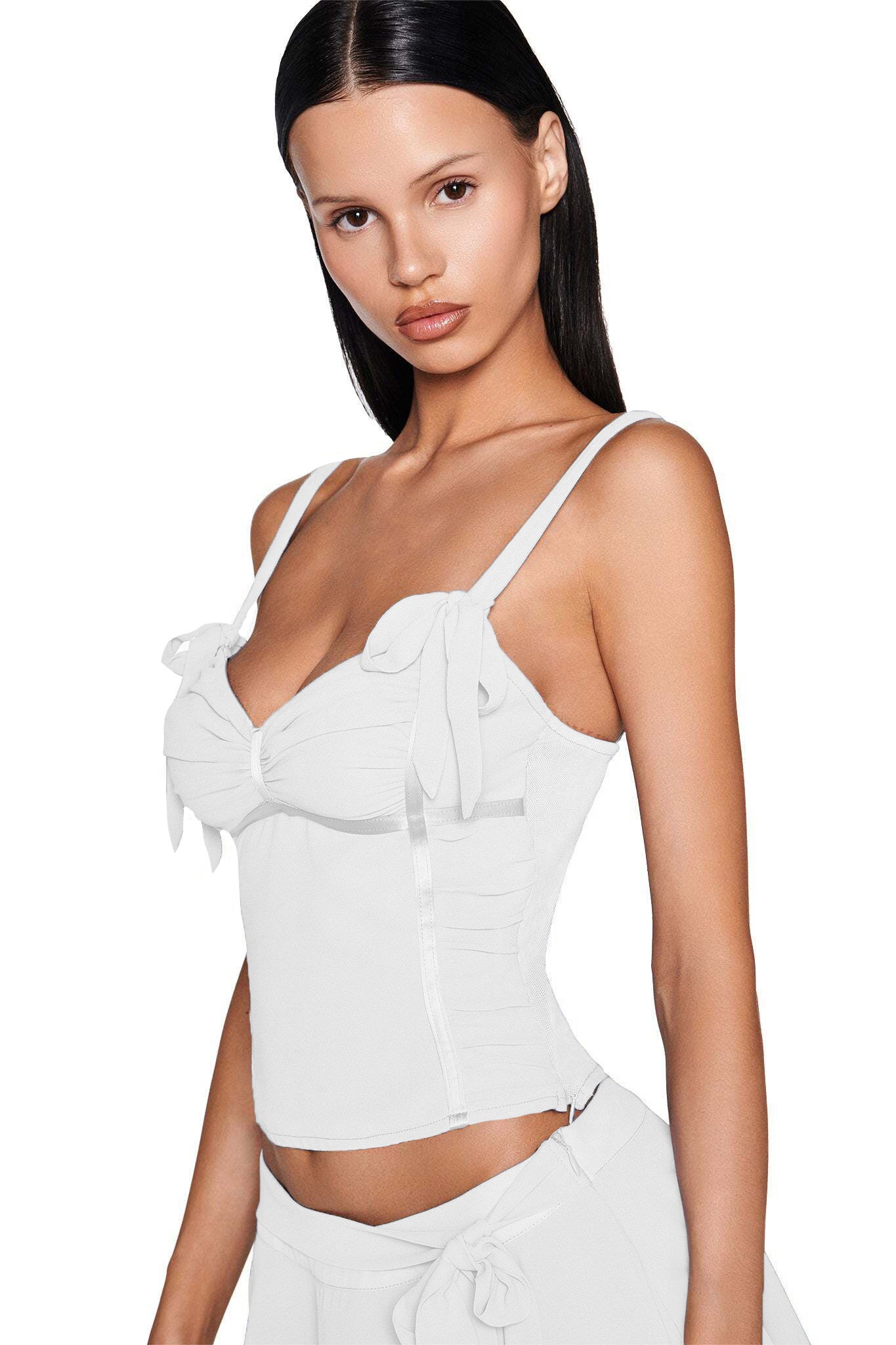 A woman with straight dark hair models the fitted white QUEENIE TOP by I.AM.GIA, featuring bow strap details, paired with a matching skirt against a plain white background.