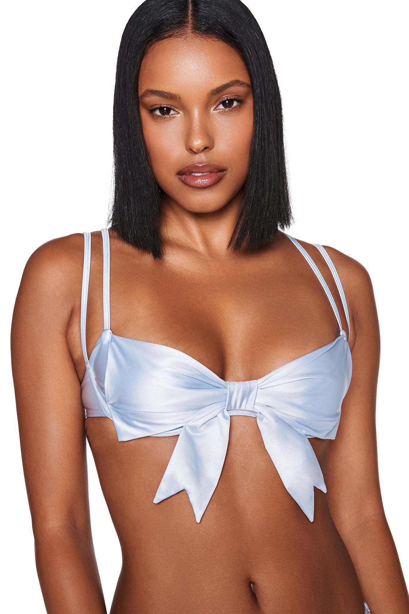A person sporting the DELPHINA BIKINI TOP - BLUE : BABY BLUE by I.AM.GIA, featuring a large front bow in light blue satin, is displayed. They have straight black hair and a neutral expression against a plain white background.