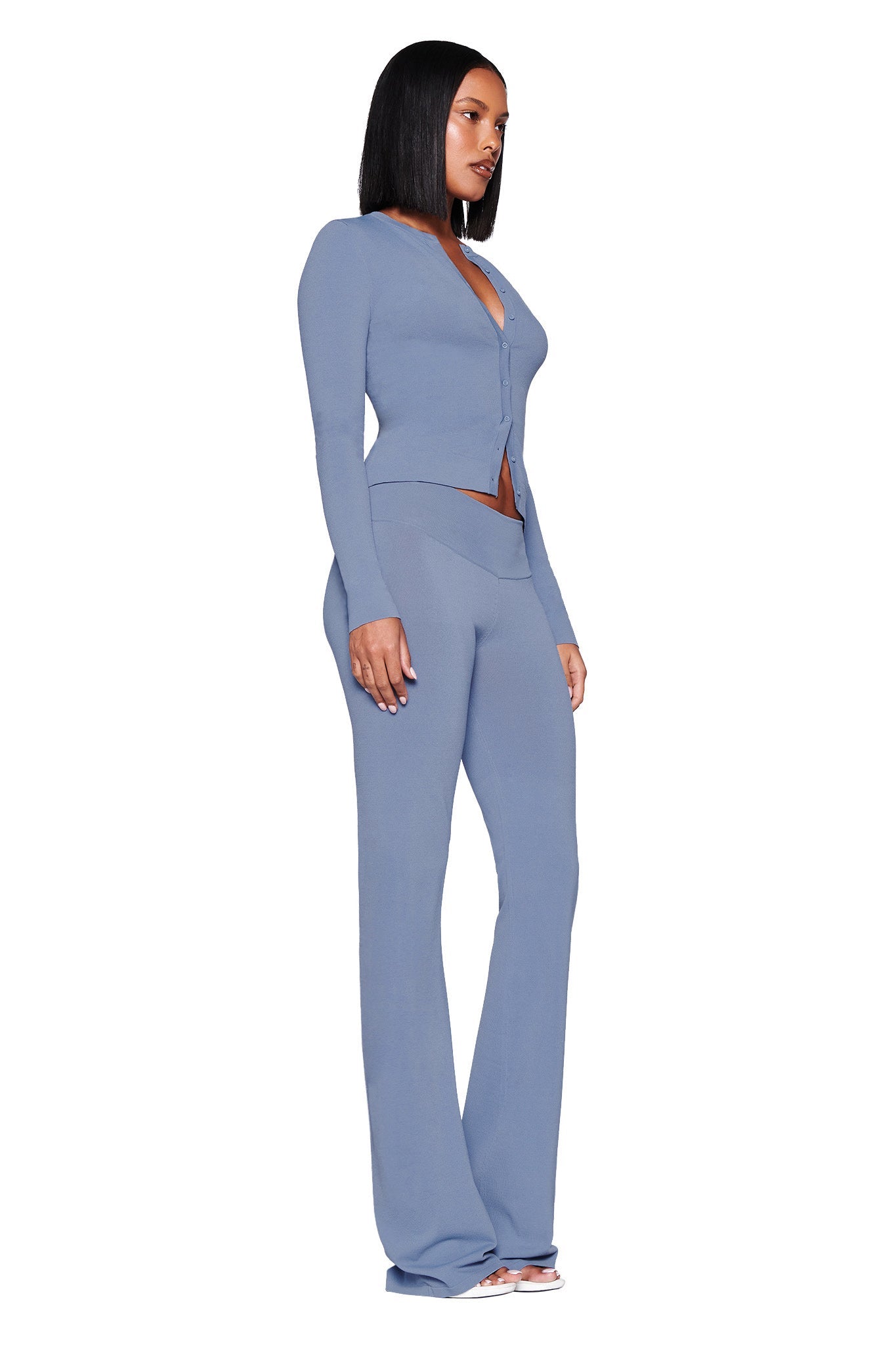 A woman poses in I.AM.GIA's AUDRINA CARDIGAN 2.0 - BLUE: STEEL BLUE, styled with matching flared knit pants and high heels, against a white backdrop.