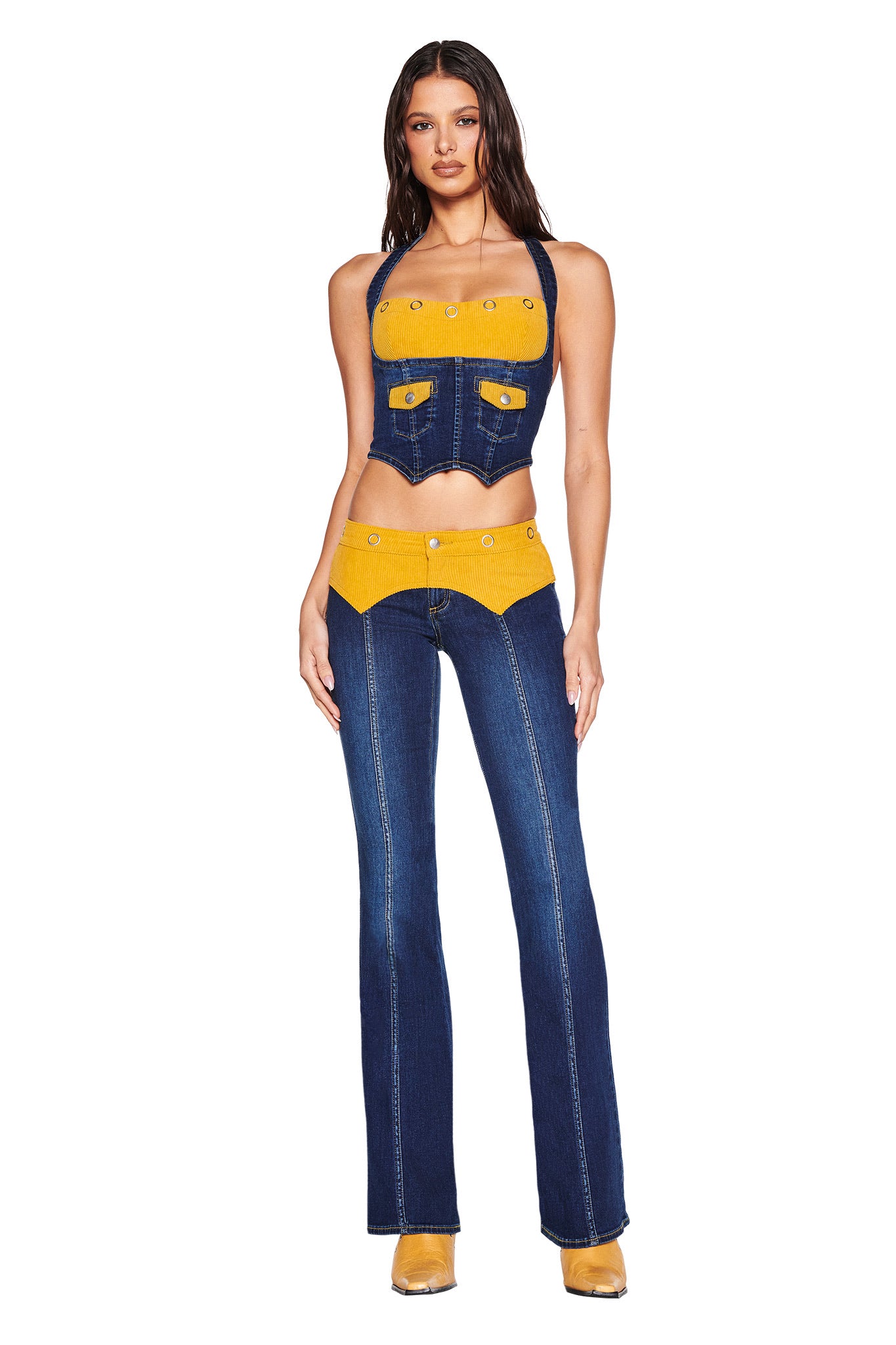 A woman faces forward in I.AM.GIA’s TOMMIE JEAN - DARK WASH set: a halter crop top and flared denim pants with mustard yellow corduroy waistband, yellow patches, button details, GIA embroidery logo, and matching yellow shoes.