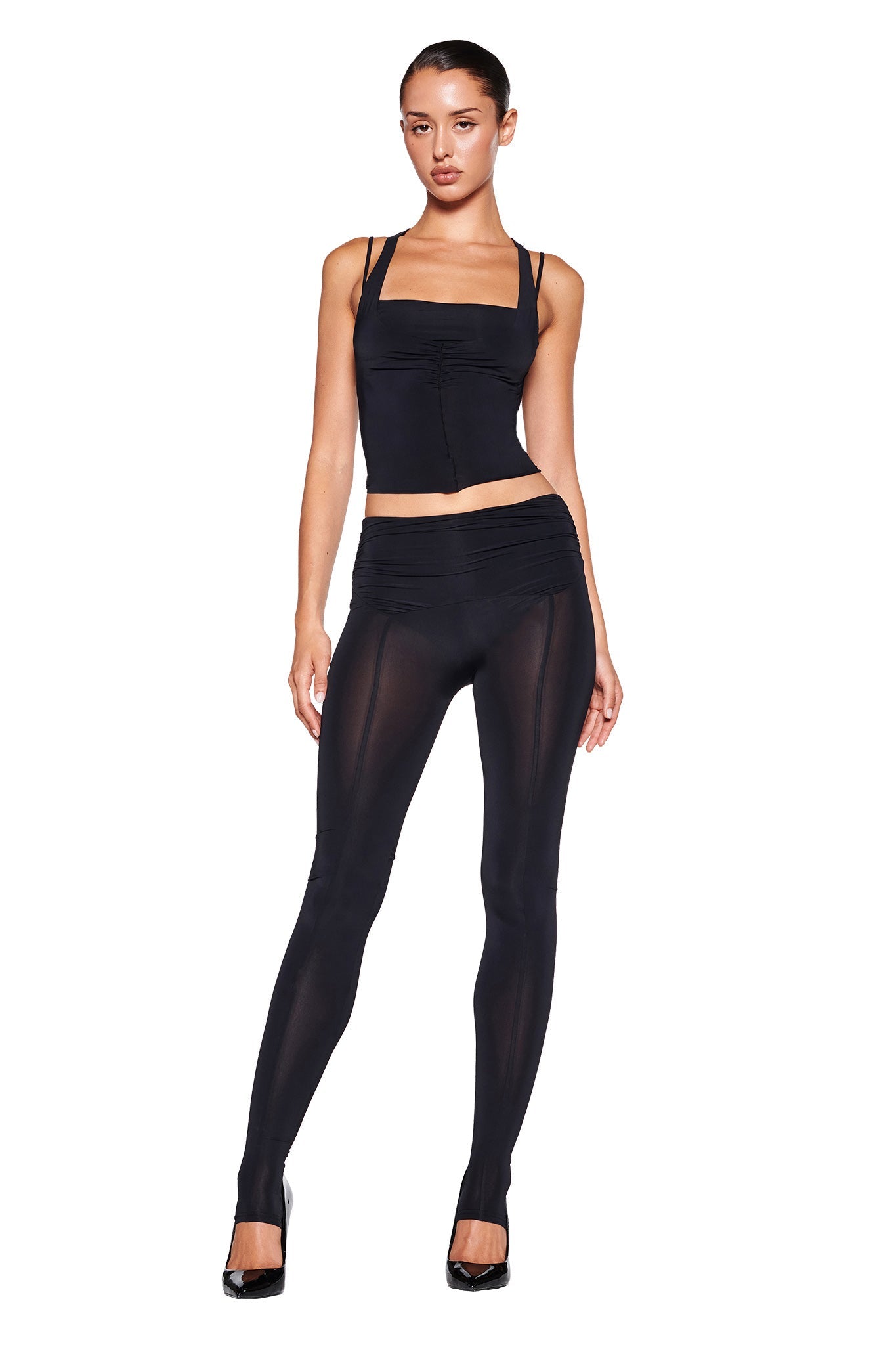 Image of the NERINA TIGHTS - BLACK by I.AM.GIA. These high-waisted leggings feature a bodycon fit with smooth, slightly sheer fabric on the lower legs. The wide waistband is ruched at the sides for added detail, providing a sleek and snug fit designed for both comfort and style.