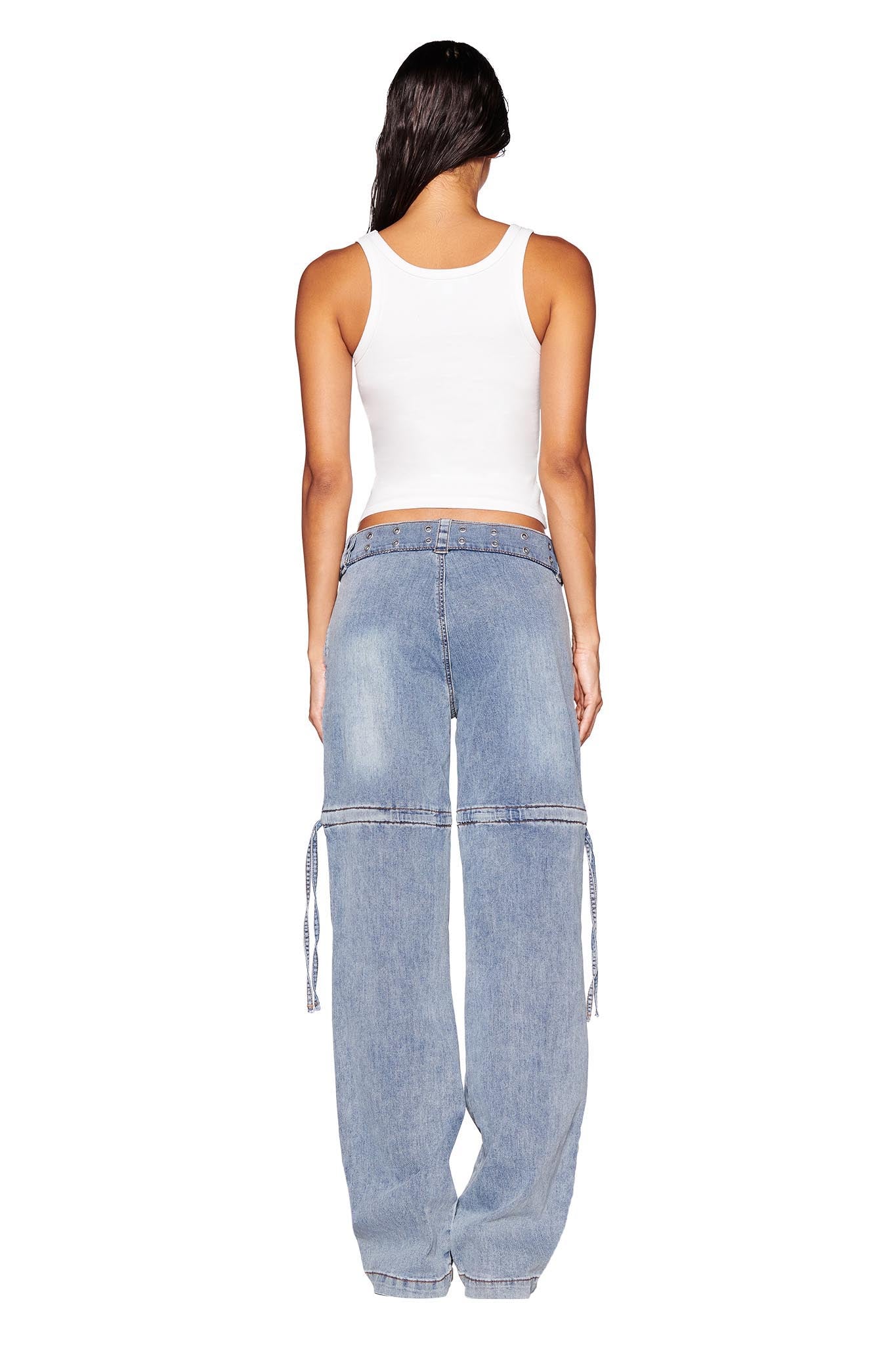 A person with long dark hair is standing facing away, wearing a white sleeveless top and light blue NAIMA CARGO PANT - DENIM by I.AM.GIA, featuring a relaxed silhouette with drawstring details on the back pockets and ankle cuffs. The background is plain white.