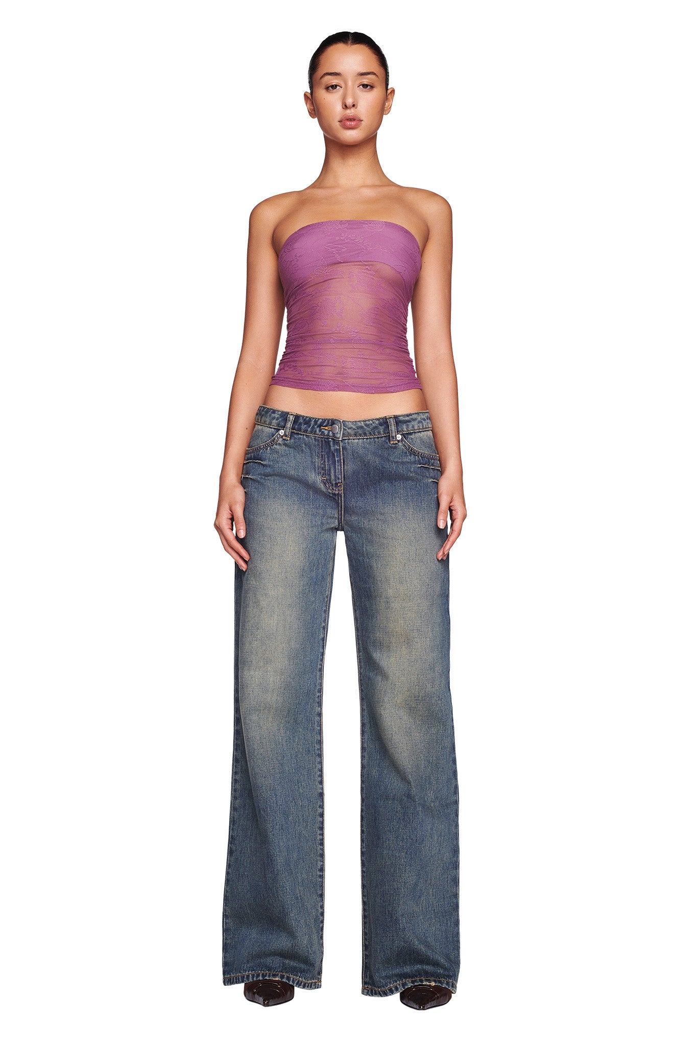 A person stands against a plain white background, wearing a strapless, sheer purple top by I.AM.GIA and the DYLAN JEAN in blue denim by I.AM.GIA. They have a neutral expression, with arms relaxed by their sides.