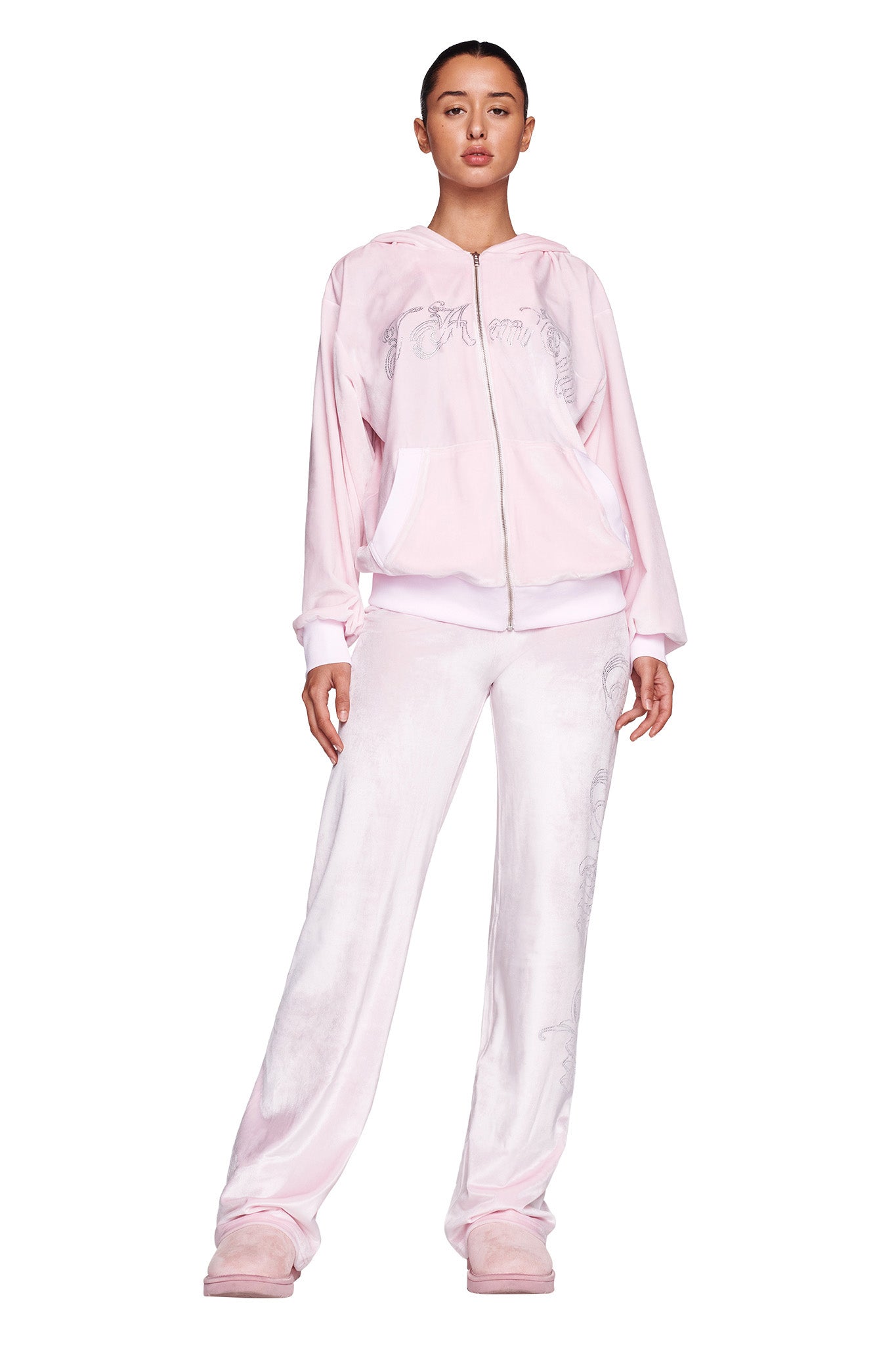 A woman is standing and facing forward, wearing the I.AM.GIA Daria Hoodie in Icy Pink with a zipper, matching pink pants, and pink shoes. The outfit appears to be casual and comfortable.
