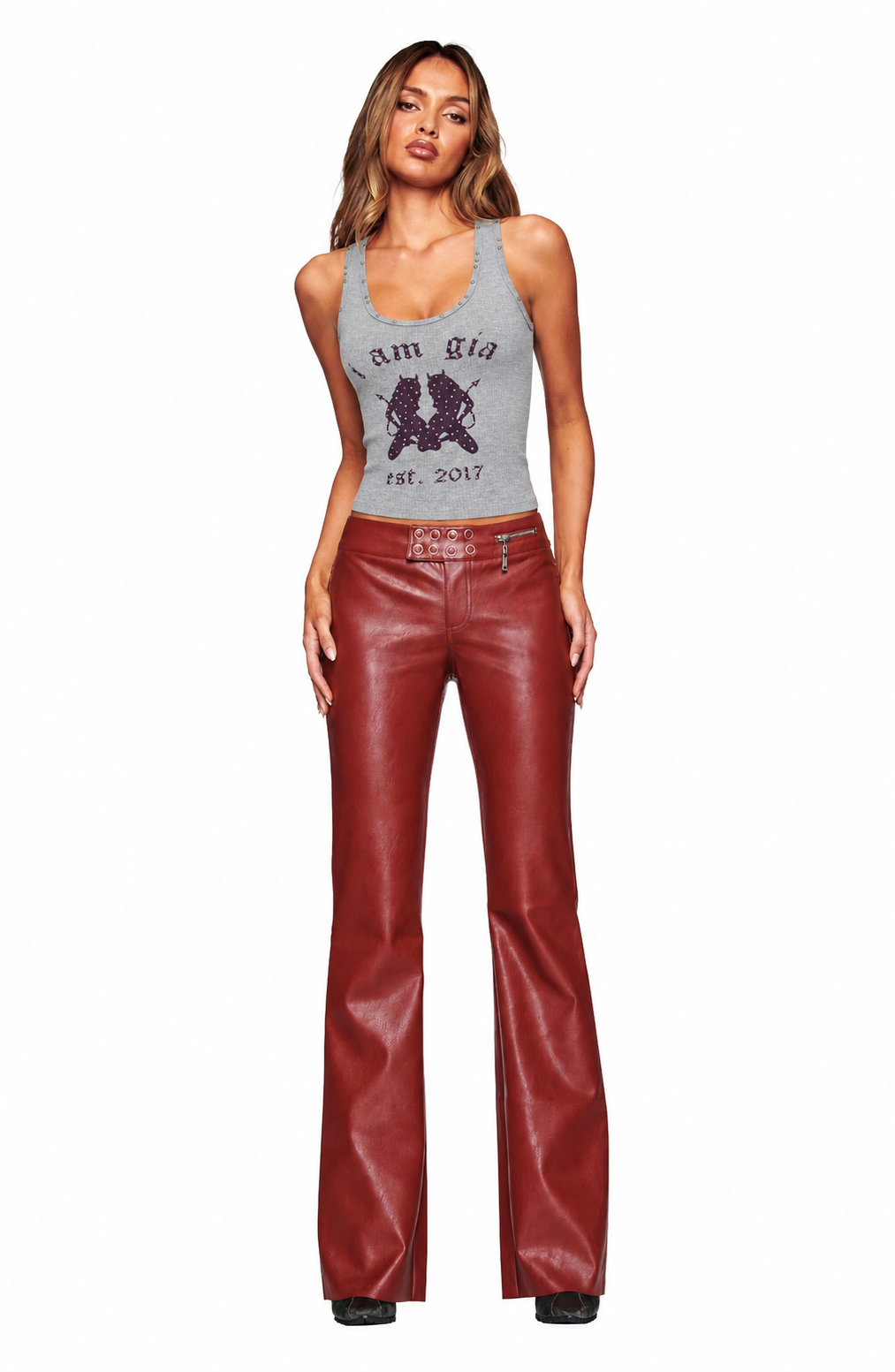 A woman faces forward in a grey sleeveless top with "I AM GIA est. 2017" and a graphic, paired with I.AM.GIA REIKA PANT - DARK RED slim fit faux leather low rise flare pants and black shoes, set against a white background.