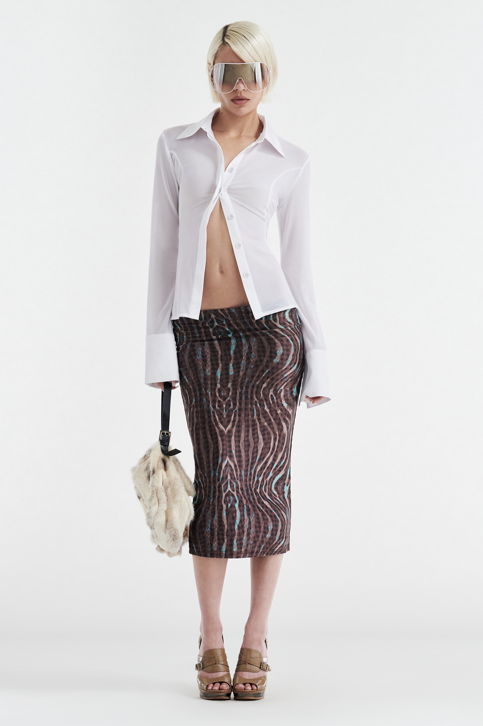 A person with short blonde hair wears oversized sunglasses, a white open button-up shirt, platform sandals, carries a furry handbag, and styles the CDP GISELLE STRETCH MIDI TUBE SKIRT - WARPED CHECK against a plain white background.