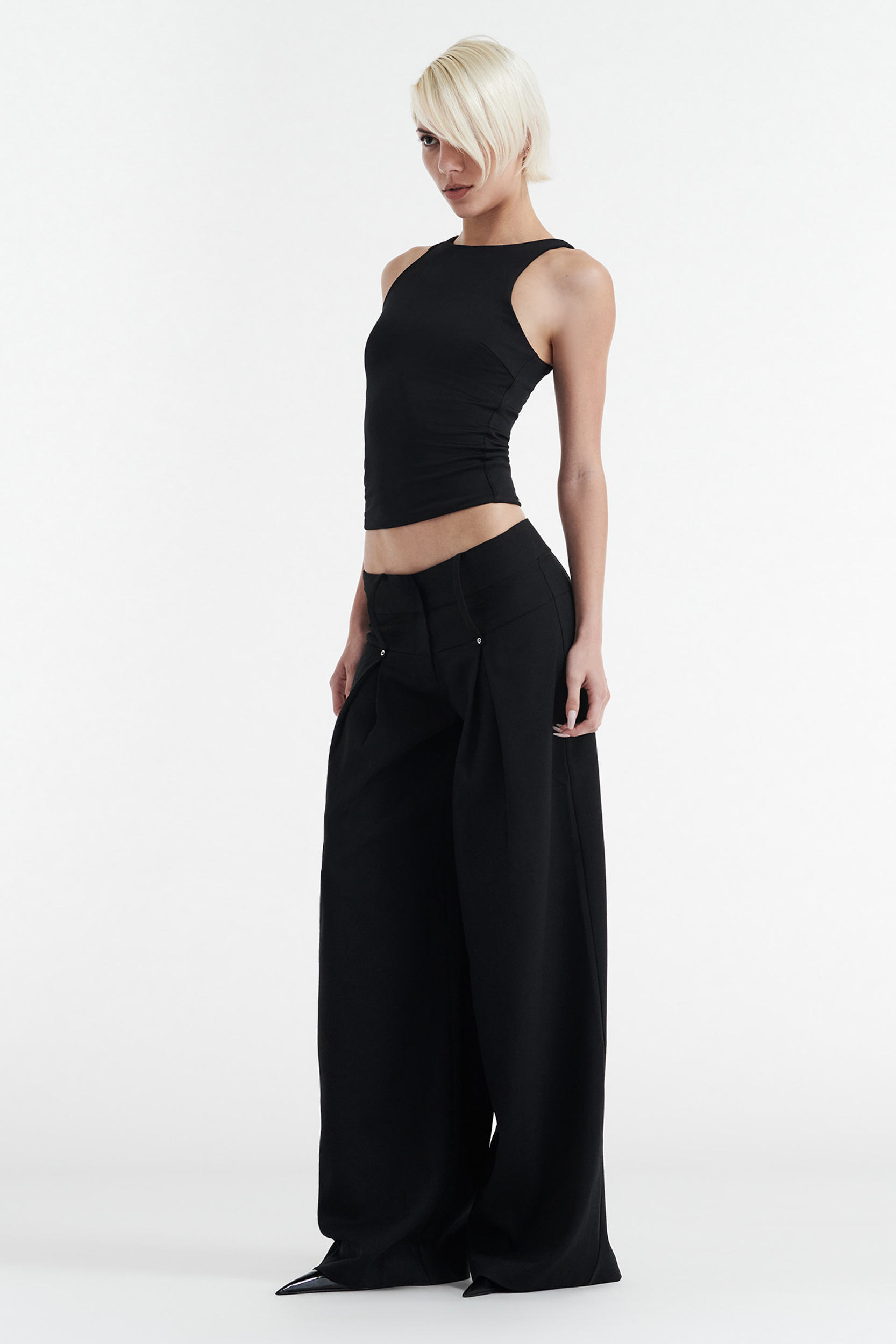 A person with short, platinum blonde hair wears the CDP SOPHIE BASIC SLEEVELESS TANK WITH SHELF BRA in black and high-waisted, wide-leg black pants, standing against a plain white background.
