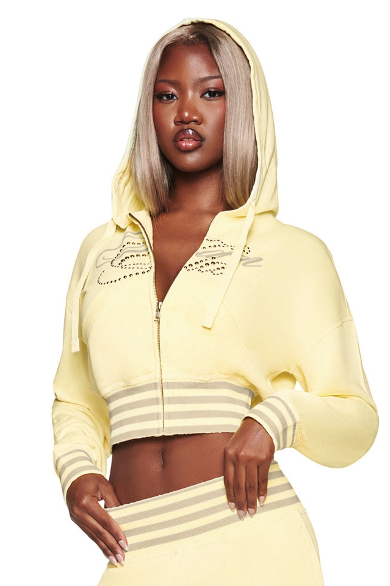 A woman with straight blonde hair and a confident expression poses with the hood up, wearing the I.AM.GIA VEDA JACKET in yellow. Crafted from soft cotton-blend fleece, this zip-up hoodie features striped cuffs and delivers both comfort and style to her look.