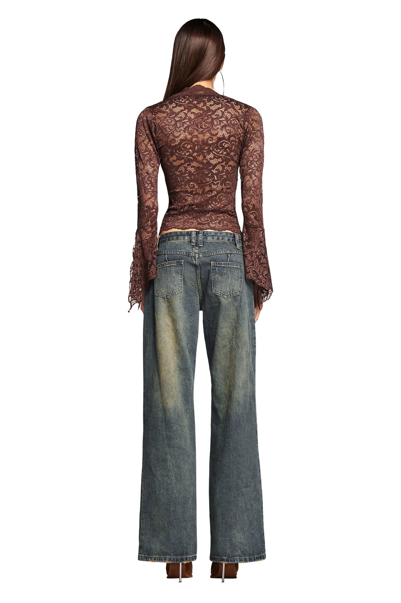Rear view of a person with long brown hair wearing the I.AM.GIA GEMMA Top in chocolate, a fitted sheer lace long-sleeve top, paired with wide-leg blue jeans featuring a faded effect. The individual is standing, showcasing the detailed lace pattern of the top and the relaxed fit of the jeans.