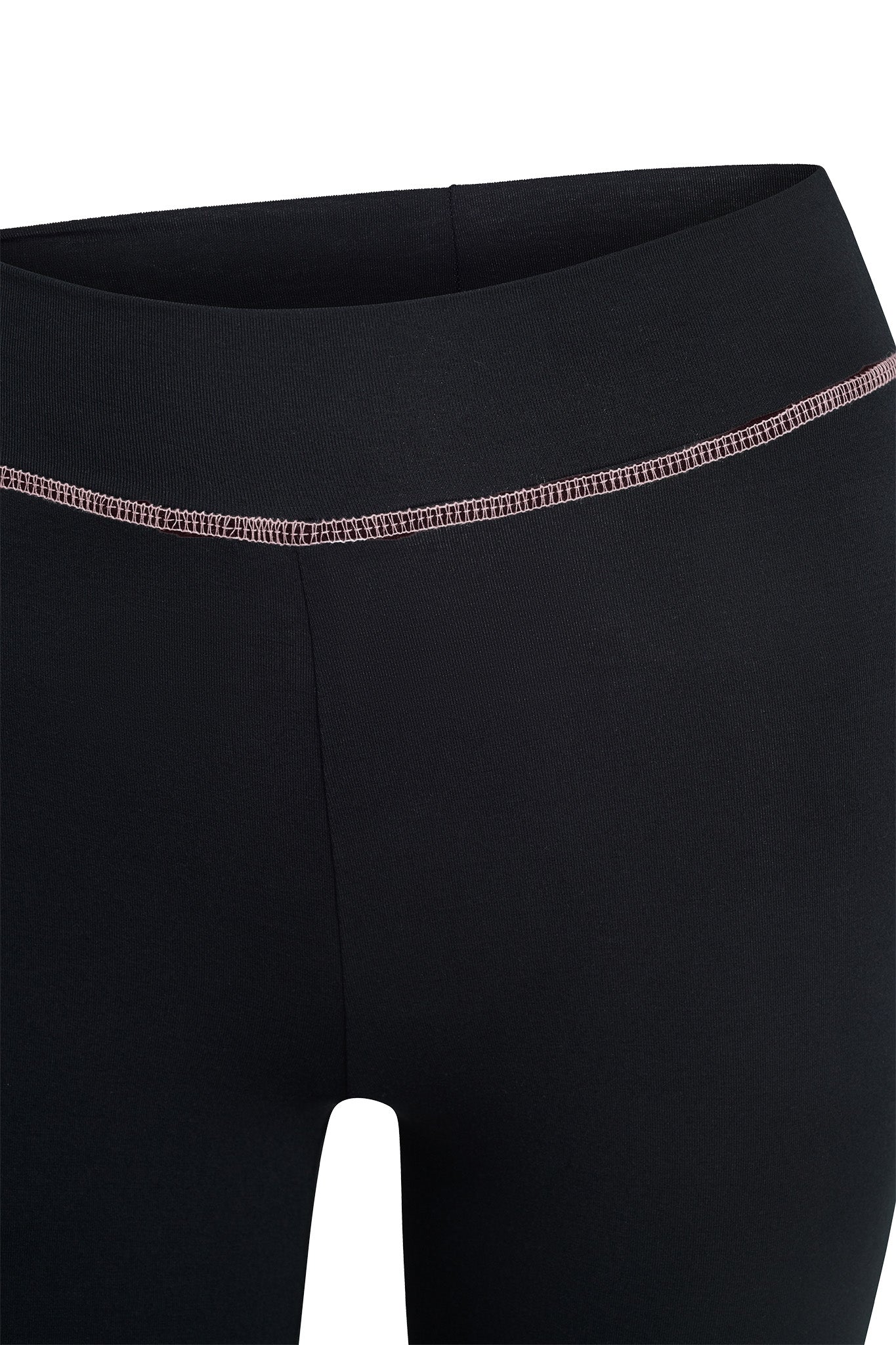 A close-up of a person wearing the I.AM.GIA BLARE TRACKPANT in black, showcasing the upper part with a visible seam around the waistband. The seam features contrasting light pink thread. The white background accentuates the black fabric.