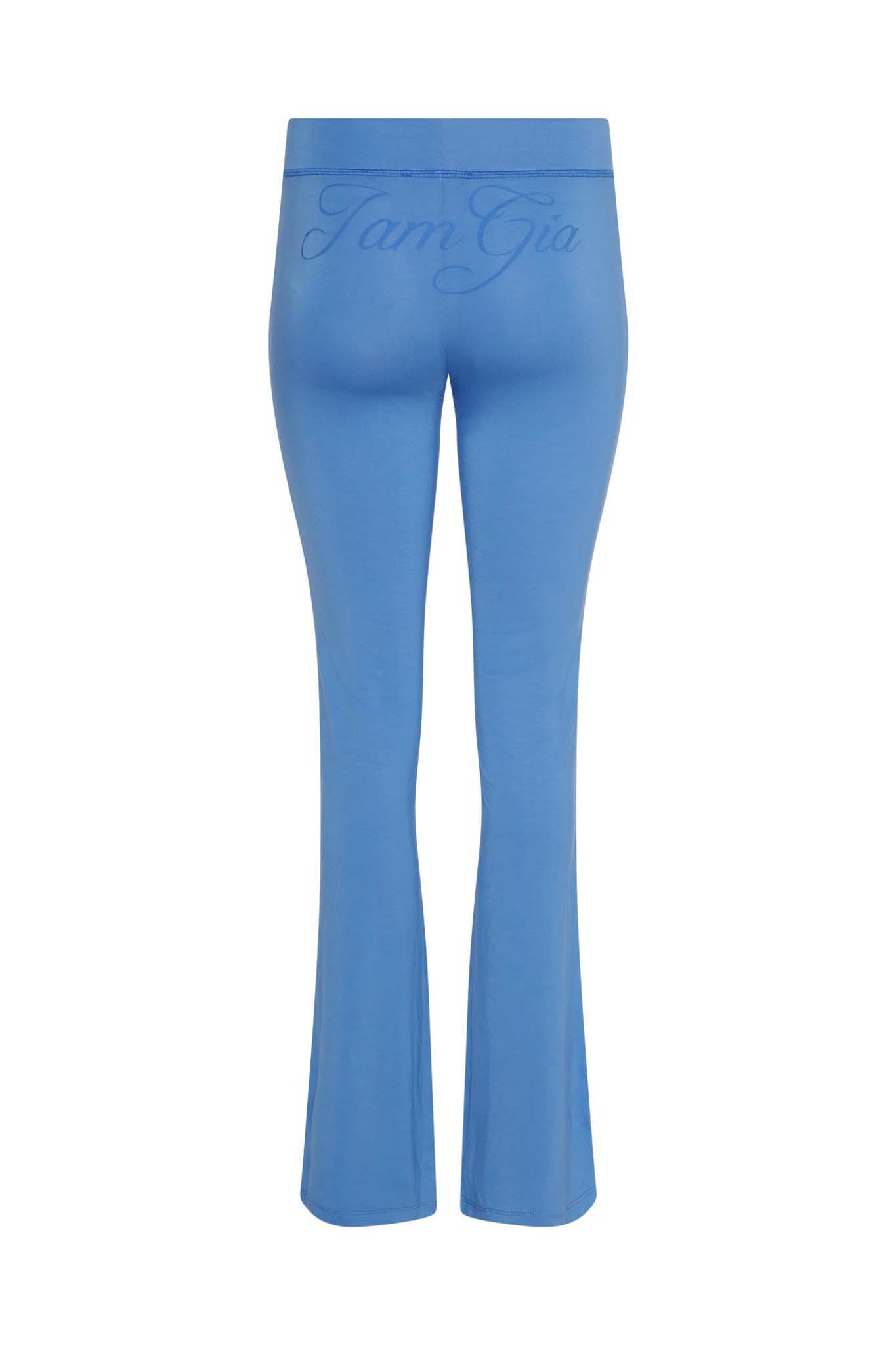 The image depicts the BLARE TRACKPANT - BLUE from I.AM.GIA, showcasing a pair of high-waisted, flared pants in blue as seen from the back. The brand name "I.AM.GIA" is subtly emblazoned across the waistband in a matching blue hue.