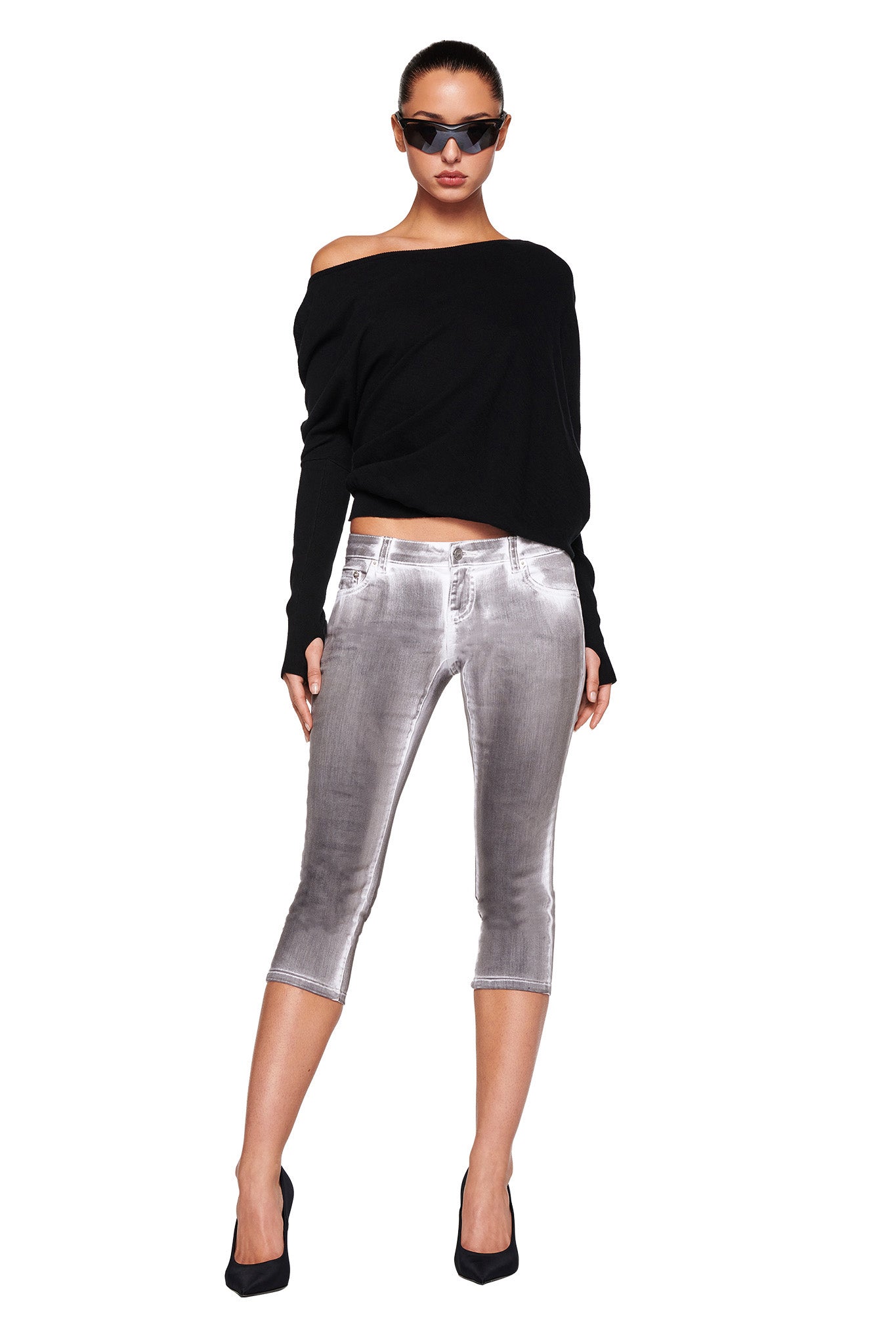 A person stands confidently wearing the GISELLE TOP - BLACK from I.AM.GIA, paired with shiny silver cropped pants, black heels, and sunglasses. They have their hands relaxed by their sides and look straight ahead against a plain white background.