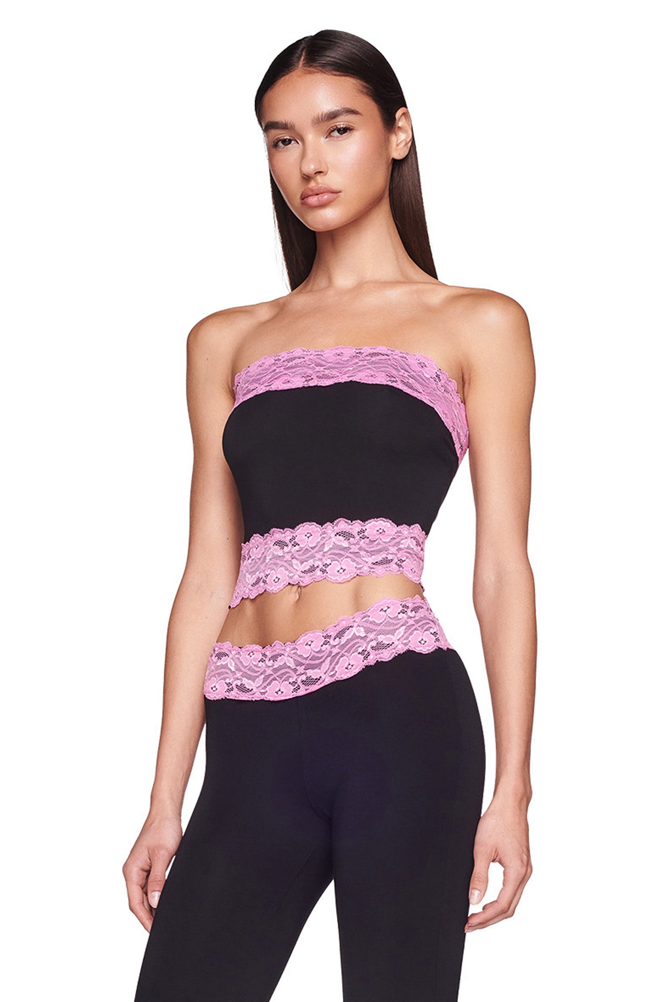 A woman with long straight hair is wearing the TARSHA BOOB TUBE - BLACK/PINK by I.AM.GIA. The form-fitting ensemble features pink lace accents at the neckline, hem, and around the waist of the strapless top. She is standing against a plain white background, looking forward with a neutral expression.