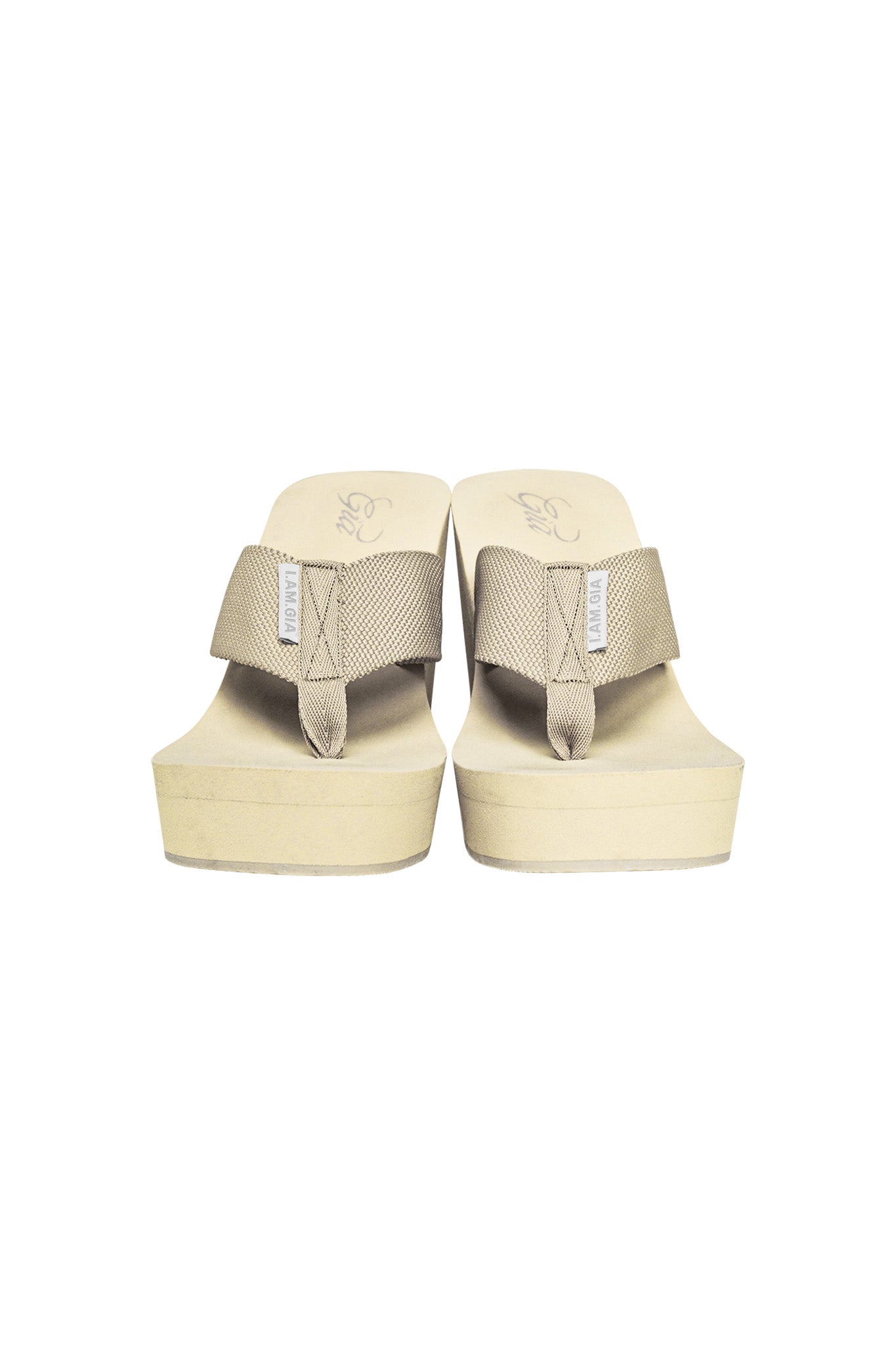 The SHELBY FLIP FLOP - NEUTRAL : TAN by I.AM.GIA is a pair of beige wedge flip-flops featuring thick, fabric thong straps with visible stitching details. The design includes a thick sole with a slight platform and top insoles adorned with a minimalistic I.AM.GIA logo, offering a casual and comfortable look.