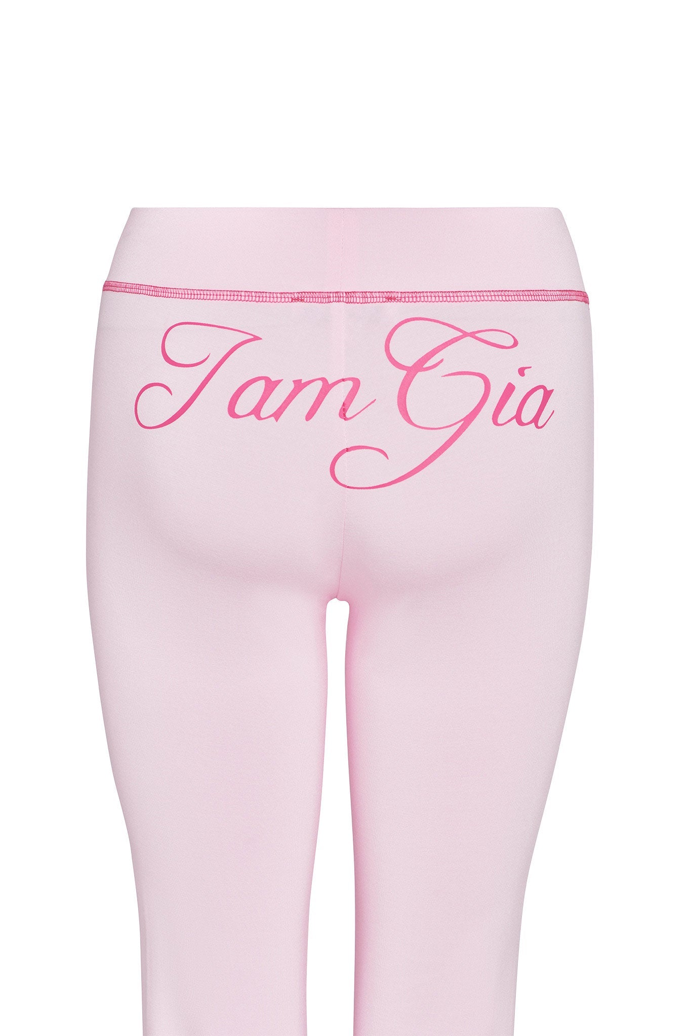 The image shows the back view of a person wearing I.AM.GIA's BLARE TRACKPANT - PINK in pastel pink, with "I.AM.GIA" elegantly written in cursive font across the top of the waistband.